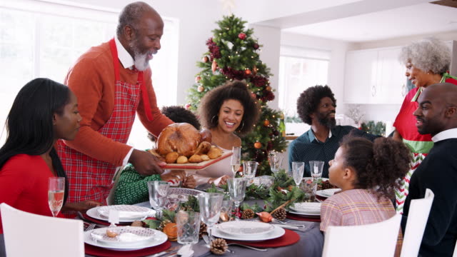 Großvater-bringt-einen-Truthahn-auf-den-Tisch-während-einer-Multi-Generation,-gemischte-Rennen-familiäre-Weihnachtsfeier