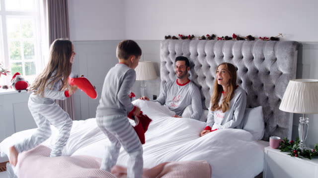 Los-niños-entusiasmados-corriendo-hacia-el-dormitorio-de-los-padres-en-casa-con-medias-y-rebotar-en-la-cama-como-familia-abren-regalos-el-día-de-Navidad