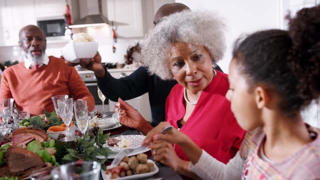 Black-senior-woman-talking-with-her-granddaughter-while-they-eat-with-their-family-at-the-Christmas-dinner-table,-close-up,-side-view