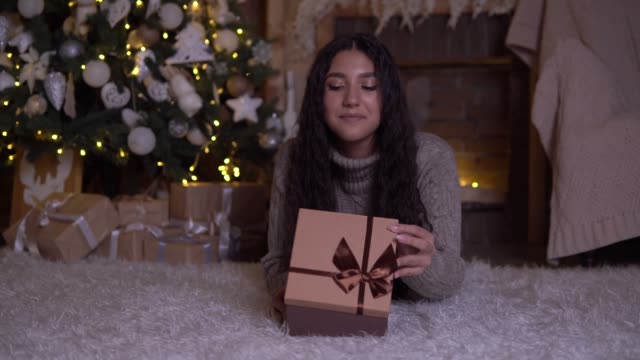 The-girl-opens-the-box-with-a-gift-and-rejoices-lying-on-the-floor-near-the-Christmas-tree.-4K
