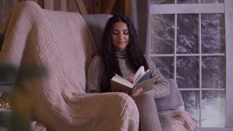 Una-niña-está-leyendo-un-libro-sentado-en-una-silla-cerca-del-árbol-de-Navidad.