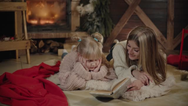 Merry-Christmas-and-Happy-New-Year.-Beautiful-family-in-Xmas-interior.-Pretty-young-mother-reading-a-book-to-her-daughter-near-Christmas-tree
