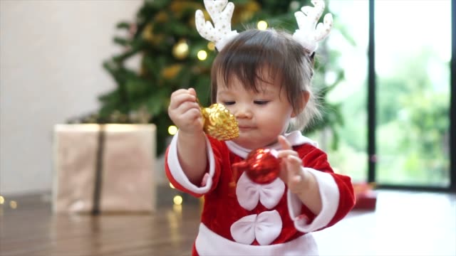 Niedliche-1-Jahr-alt-Baby-Mädchen-tragen-Rentier-Haarreif-mit-Christbaumkugel-mit-Weihnachtsbaum-im-Hintergrund-zu-spielen.-Frohe-Weihnachten-und-schöne-Feiertage!