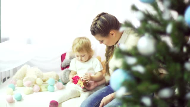 Madre-joven-feliz-jugando-con-su-bebé-dulce-en-un-decorado-cerca-del-árbol-de-Navidad