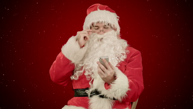 Santa-claus-liest-und-sendet-Textnachrichten-von-seinem-Handy-auf-rotem-Hintergrund-mit-Schnee