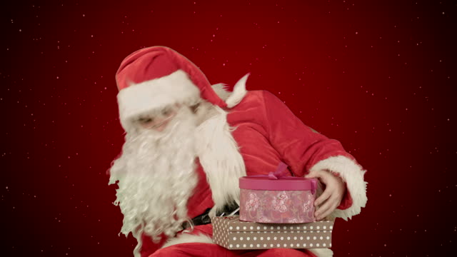 Santa-Claus-sosteniendo-un-regalo-en-su-mano-sobre-fondo-rojo-con-nieve