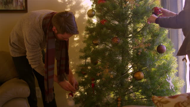 Joven-marido-y-mujer-poniendo-adornos-en-un-árbol-de-Navidad