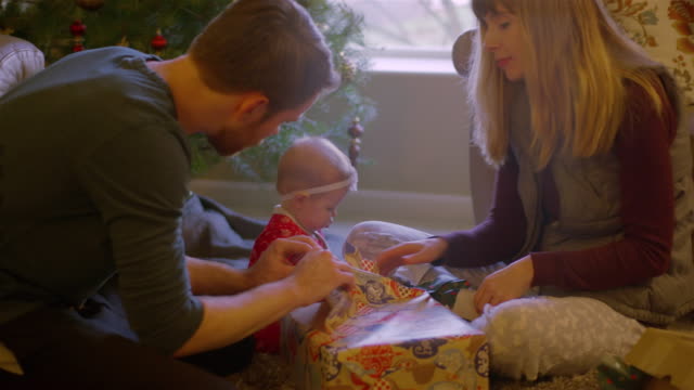 Eltern-öffnen-geschenke-mit-ihrem-Baby-vor-dem-Baum-am-Weihnachtsmorgen