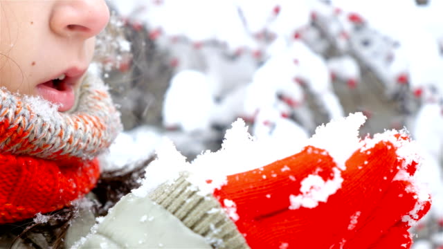 Close-up-of-girl-in-red-scarf-and-gloves-blowing-snow