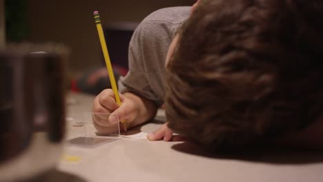 Ein-Junge-sitzt-an-der-Küchentheke,-schreibt-und-legt-einen-Weihnachtsaufkleber-auf-ein-Blatt-Papier