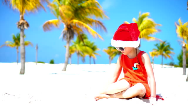 Pequeña-niña-adorable-en-rojo-sombrero-de-Santa-en-la-playa-tropical-en-las-vacaciones-de-Navidad