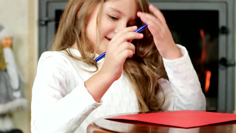 little-girl-writes,-the-child-draws-pen-on-sheet-of-paper,-cute-girl-sitting-near-fireplace-where-fire-is-burning-at-wooden-table-in-living-room-at-home