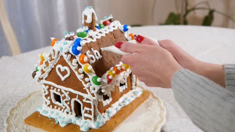 The-woman-writes-a-text-with-cream-on-the-roof-of-gingerbread-house