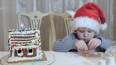 Cute-little-boy-in-santa's-hat-palys-with-colorful-candies-at-the-table