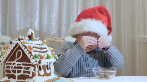 Niedlichen-kleinen-Jungen-in-die-Weihnachtsmütze-schält-eine-Süßigkeit-aus-Schokolade-in-der-Küche