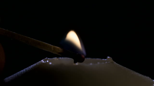 Slow-motion-macro-footage-of-a-white-candle-lit-by-a-match-on-a-dark-background