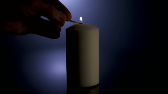 Slow-Motion-Makro-Aufnahmen-von-einer-weißen-Kerze-beleuchtet-durch-ein-Match-auf-einem-dunklen-Hintergrund