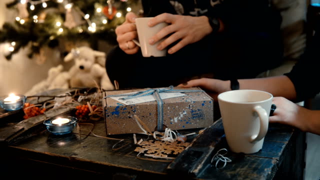 Nahaufnahme-von-junges-Paar-sitzt-am-Tisch,-in-der-Nähe-von-den-Weihnachtsbaum-und-öffnen-Sie-die-Feiertage-vorhanden,-Tee-trinken