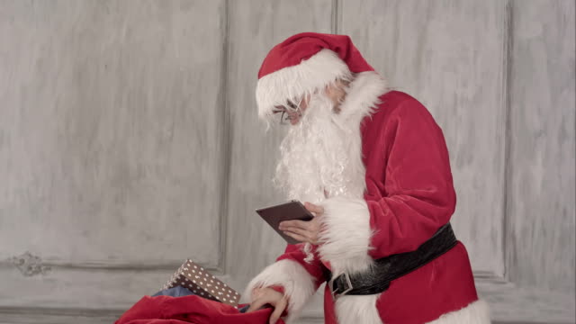Santa-Claus-mit-Tablet-pc-Computer-überprüfen-Geschenktüte