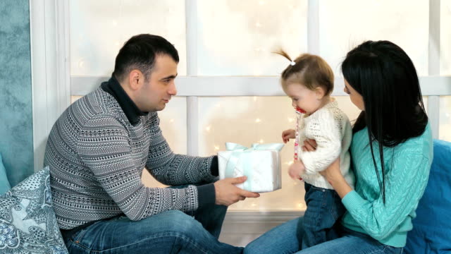 Hermosa-familia-feliz-Navidad-con-niña-en-suéteres-de-punto-sentado-en-el-alféizar-de-la-ventana