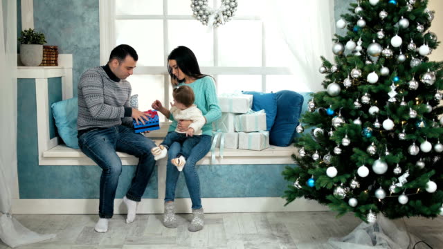 Hermosa-familia-feliz-Navidad-con-niña-en-suéteres-de-punto-sentado-en-el-alféizar-de-la-ventana