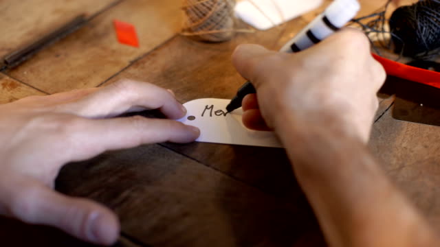 Jungen-Erwachsenen-Mannes-schreiben-Weihnachtskarte-auf-white-Label-auf-alten-Holztisch-im-Innenbereich-gemütliches-Zuhause
