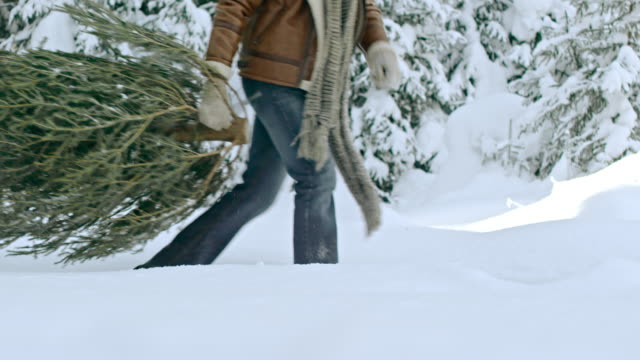 Familia-feliz-arrastrando-el-árbol-de-Navidad-en-el-bosque-nevado
