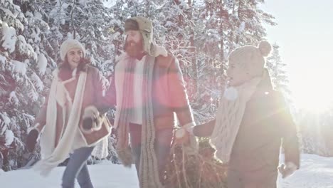 Familia-llevando-árbol-de-Navidad-a-través-de-bosque-de-invierno