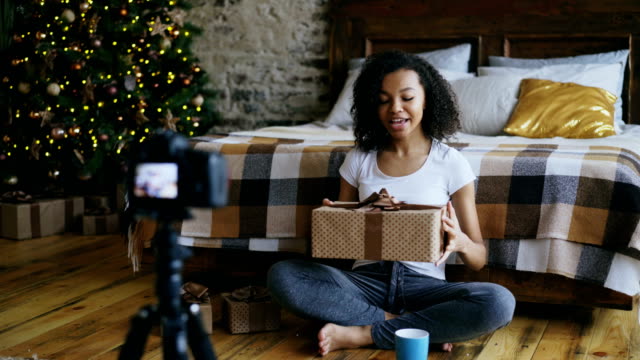 Joven-rizado-mixto-a-mujer-raza-grabación-video-blog-sobre-embalaje-caja-de-regalo-de-Navidad-en-casa