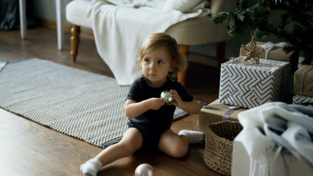 Adorable-little-girl-playing-with-toy-balls-sitting-near-Christmas-tree-at-home