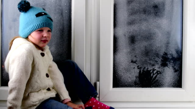 Kleine-Mädchen-sitzt-auf-der-Fensterbank-hinter-dem-gefrorenen-Fenster.-Niedrige-DOF.