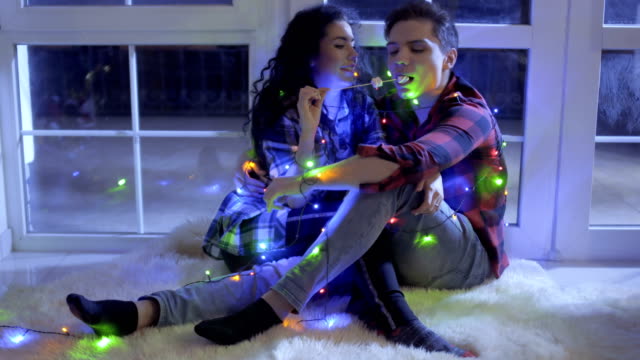 Beautiful-couple-decorated-with-christmas-garland-eats-marshmellows