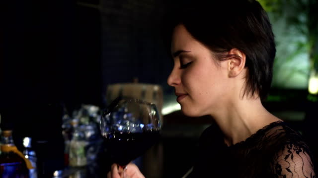 Close-up-of-a-gorgeous-brunette-enjoying-drinking-wine-at-the-bar-smiling-to-the-camera