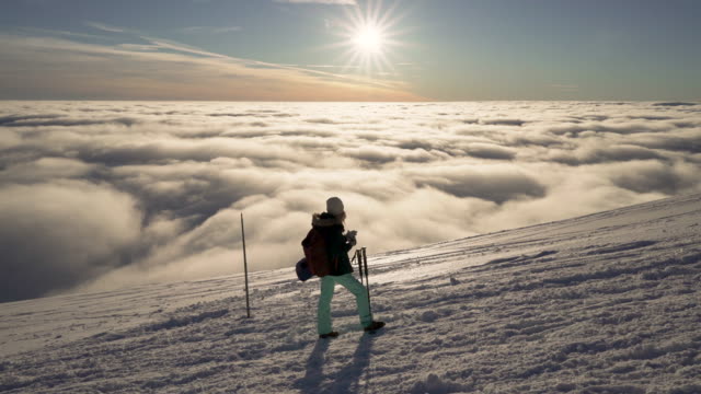 Stabilized-flow-motion-shot-of-girl-hiking-on-snow-in-Slovak-mountains-above-clouds-during-sunset-in-winter