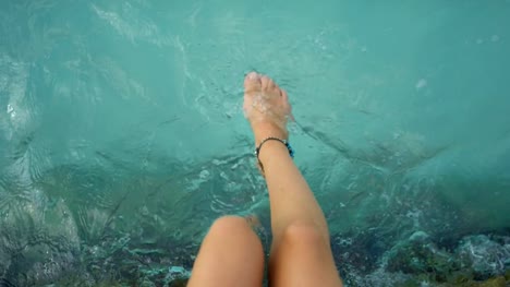 Las-piernas-de-una-mujer-sentada-en-un-muelle-y-chapoteando-en-el-mar-de-aguamarina.