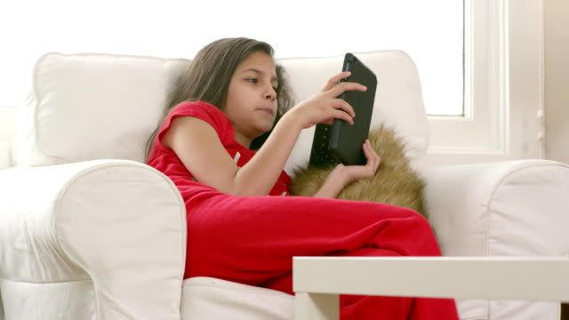Ein-Mädchen-sitzt-auf-einem-Stuhl-im-Wohnzimmer-in-ihren-Pyjamas-und-Blicke-auf-Ihr-tablet