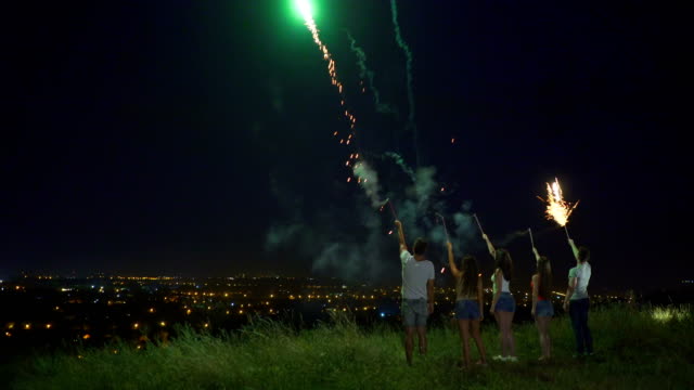 Die-fünf-Menschen-stehen-mit-Feuerwerk-Sticks-auf-einem-Stadt-Hintergrund.-Nachtzeit