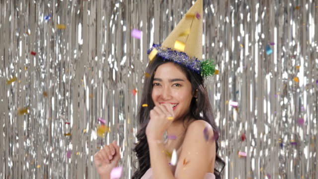 Beautiful-asian-woman-holding-glass-of-champagne-dancing-among-confetti-over-silver-glitter-background,-slow-motion