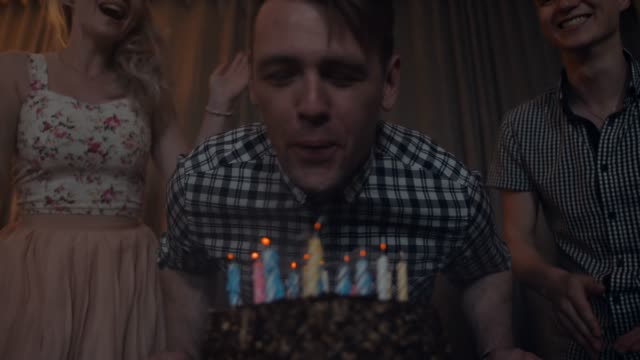Young-man-blows-out-candles-on-a-festive-cake-with-friends-near