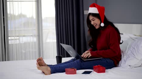 glückliche-Frau-mit-Laptop-Computer-mit-Weihnachtsgeschenk-auf-einem-Bett