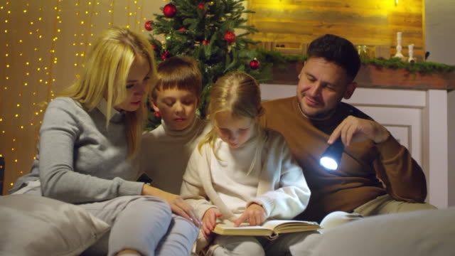 Parents-and-Kids-Reading-Fairytale-by-Christmas-Tree-at-Home