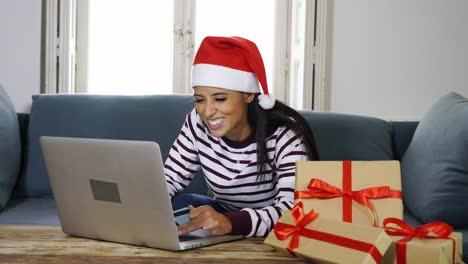Mujer-vestida-con-suéter-rojo-y-sombrero-de-santa-claus-con-tarjeta-de-crédito-elegir-y-comprar-regalos-de-Navidad-usando-laptop-en-casa-emocionado-con-ventas-por-internet-y-tarjetas-de-crédito-instalaciones-en-línea-de-compras