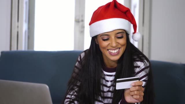 Mujer-vestida-con-suéter-rojo-y-sombrero-de-santa-claus-con-tarjeta-de-crédito-elegir-y-comprar-regalos-de-Navidad-usando-laptop-en-casa-emocionado-con-ventas-por-internet-y-tarjetas-de-crédito-instalaciones-en-línea-de-compras