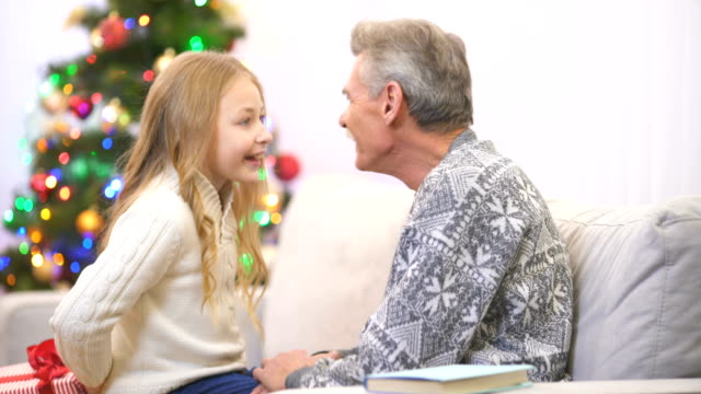 Der-Großvater-ein-Buch-lesen-und-nehmen-Sie-ein-Geschenk-von-einer-Mädchen-in-der-Nähe-der-Weihnachtsbaum