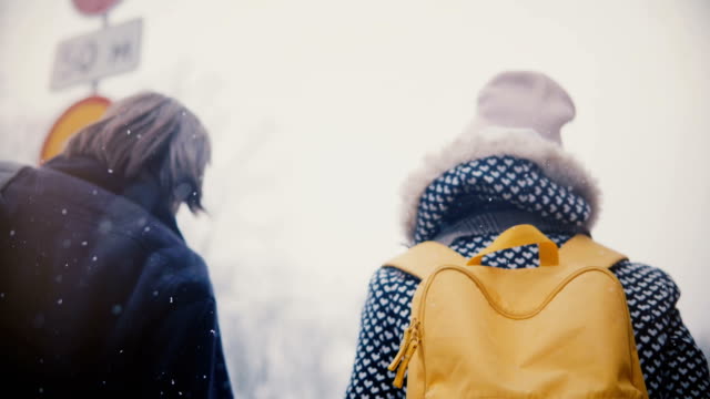 Back-view-happy-relaxed-young-man-and-woman-with-bright-yellow-backpack-walk-together-holding-hands-on-a-cold-snowy-day.