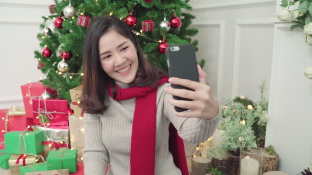 Alegre-feliz-joven-mujer-asiática-con-smartphone-selfie-de-Navidad-árbol-decorar-su-sala-de-estar-en-el-país-en-el-Festival-de-Navidad.-Mujer-de-estilo-de-vida-celebrar-Navidad-y-año-nuevo-concepto.