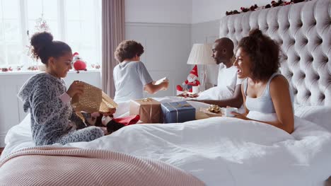 Begeistert-Kinder-in-ihre-Eltern-Schlafzimmer-laufen-und-springen-auf-ihrem-Bett-mit-Weihnachtsstrümpfe-und-Geschenken-am-Weihnachtsmorgen,-Seitenansicht