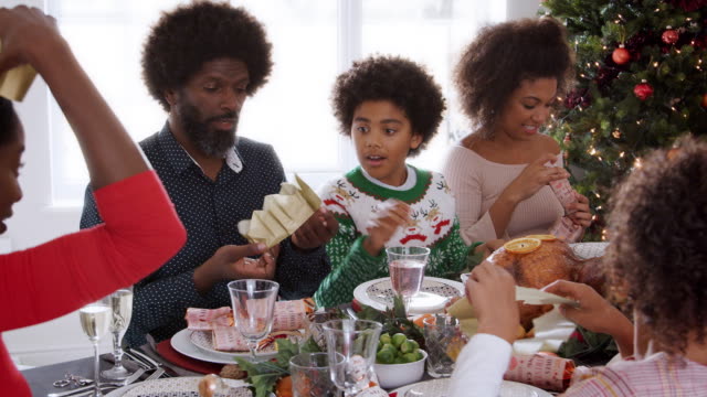 Multi-Generation,-die-gemischte-Rennen-Familie-an-Weihnachten-Abendessen-Tisch-tragen-Papier-Kronen,-panning-shot
