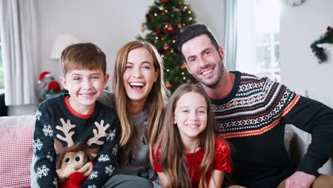 Porträt-von-Eltern-mit-Kindern-tragen-festliche-Jumper-sitzend-auf-Sofa-Lounge-zu-Hause-am-Weihnachtstag