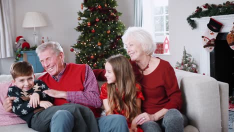 Porträt-von-Großeltern-mit-Enkeln-auf-Sofa-sitzen-In-der-Lounge-zu-Hause-am-Weihnachtstag